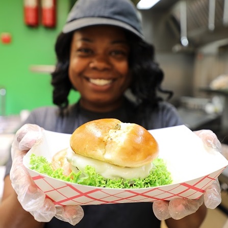 employee smiling and holding a hamburger in front