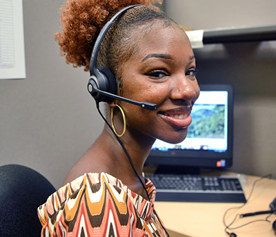 female student communication assistant wearing headphones in front of computer