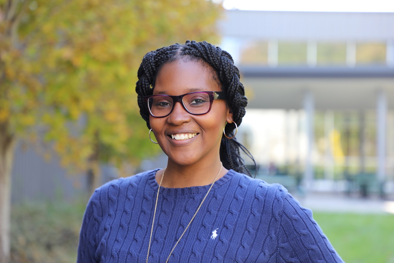 headshot of Charmaine standing outside, wearing glasses and purple sweater