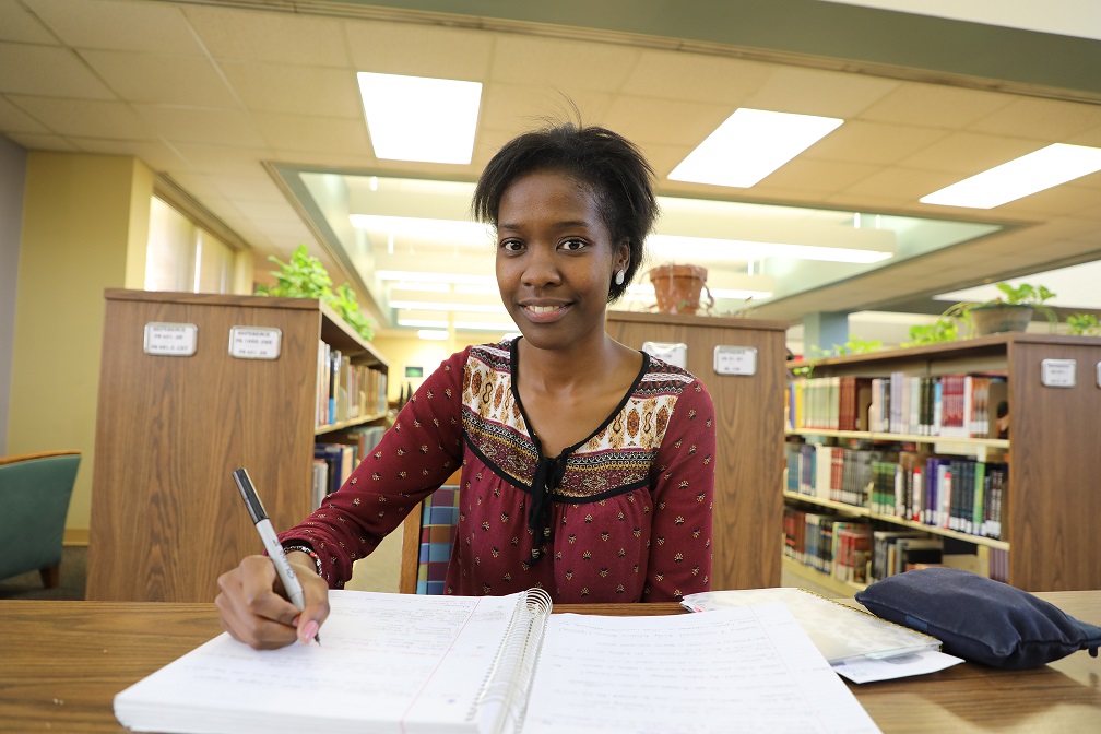 ednah sitting at table in library writing in notebook and smiling