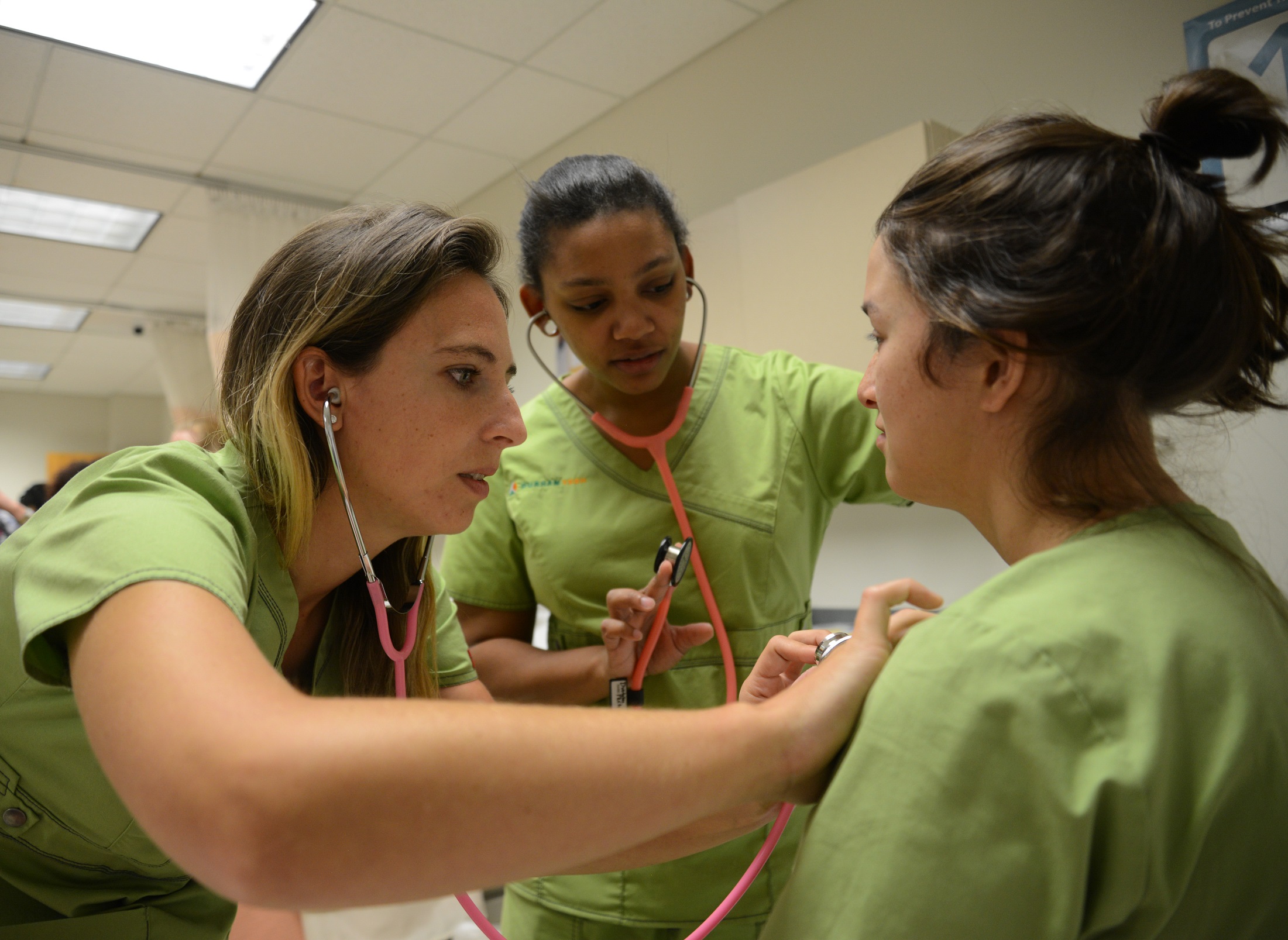 students practicing the use of a stethoscope on another student