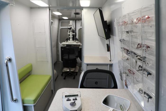 inside mobile health lab glasses on wall green seating and two chairs with tv screen on wall