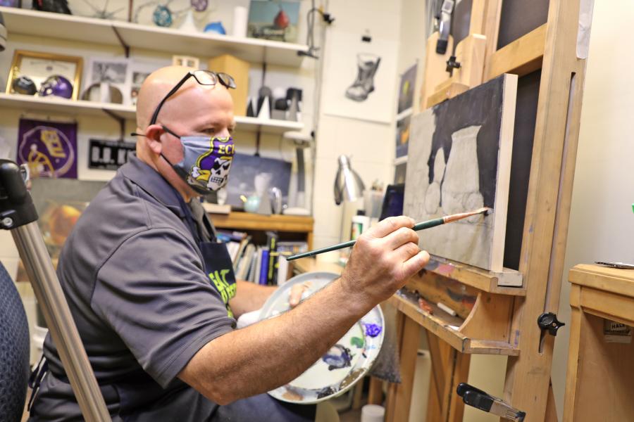 person with mask on sitting in front of easel and painting