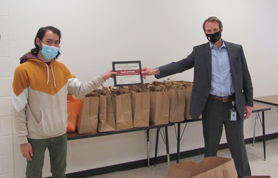 two people six feet apart each wearing a mask and holding the award in the middle