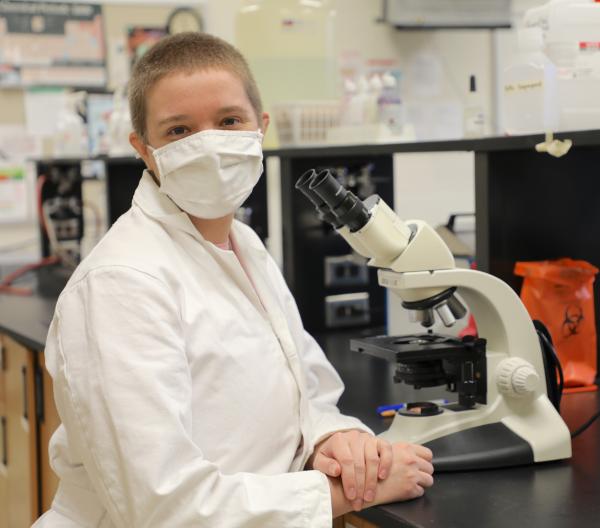 student in mask sitting in front of microscope