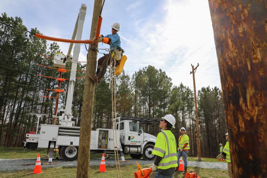 line tech students standing on ground watching another student climb a pole