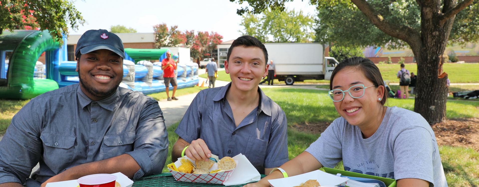 Three Durham Tech students sit in the quad at Durham Tech during a festival.