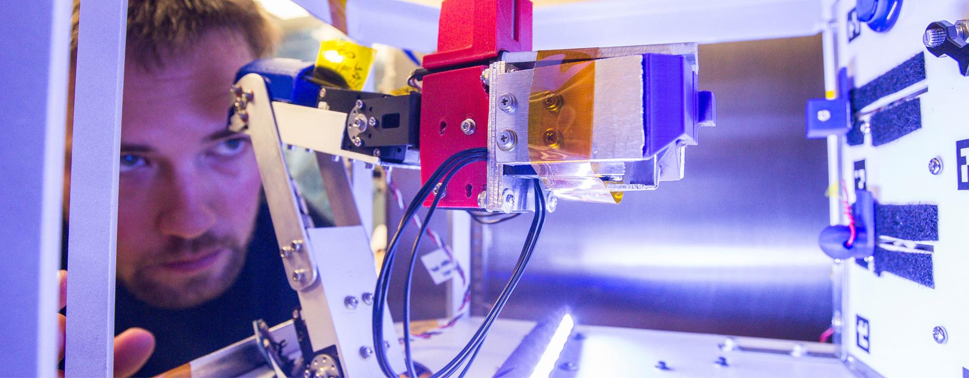student peers through machine at NASA to look at robotic arm