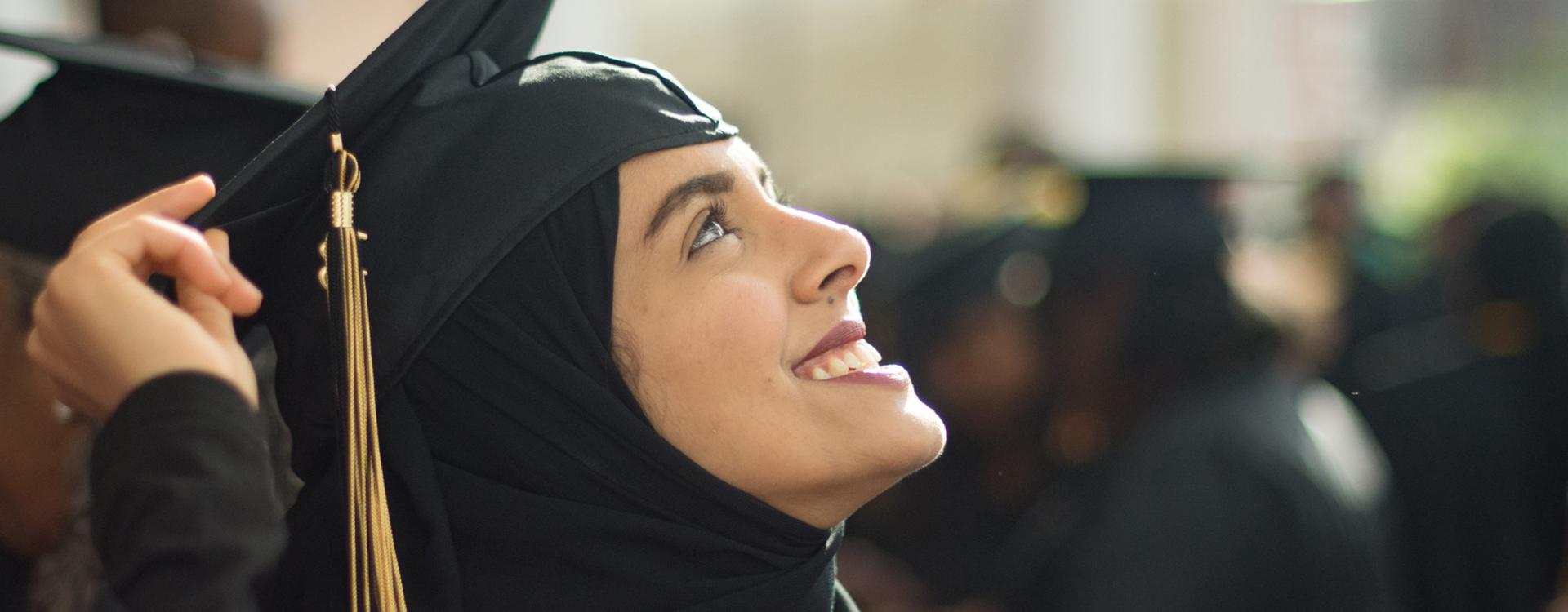 female student in graduation regalia looks up smiling