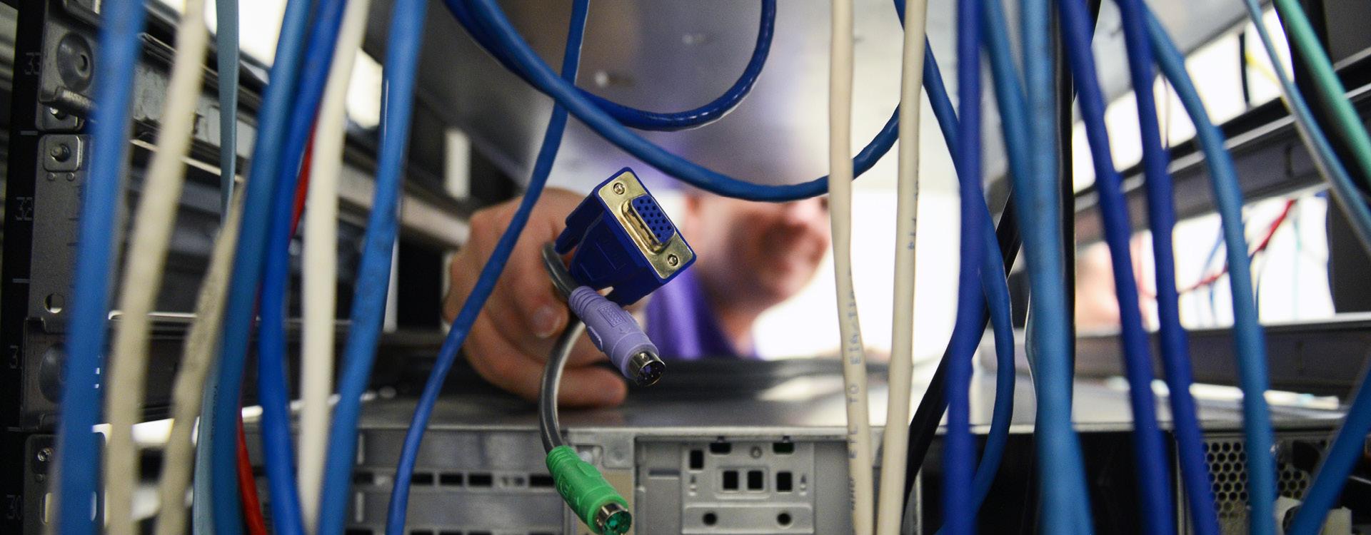 it student reaches through computer cords to the back of a server