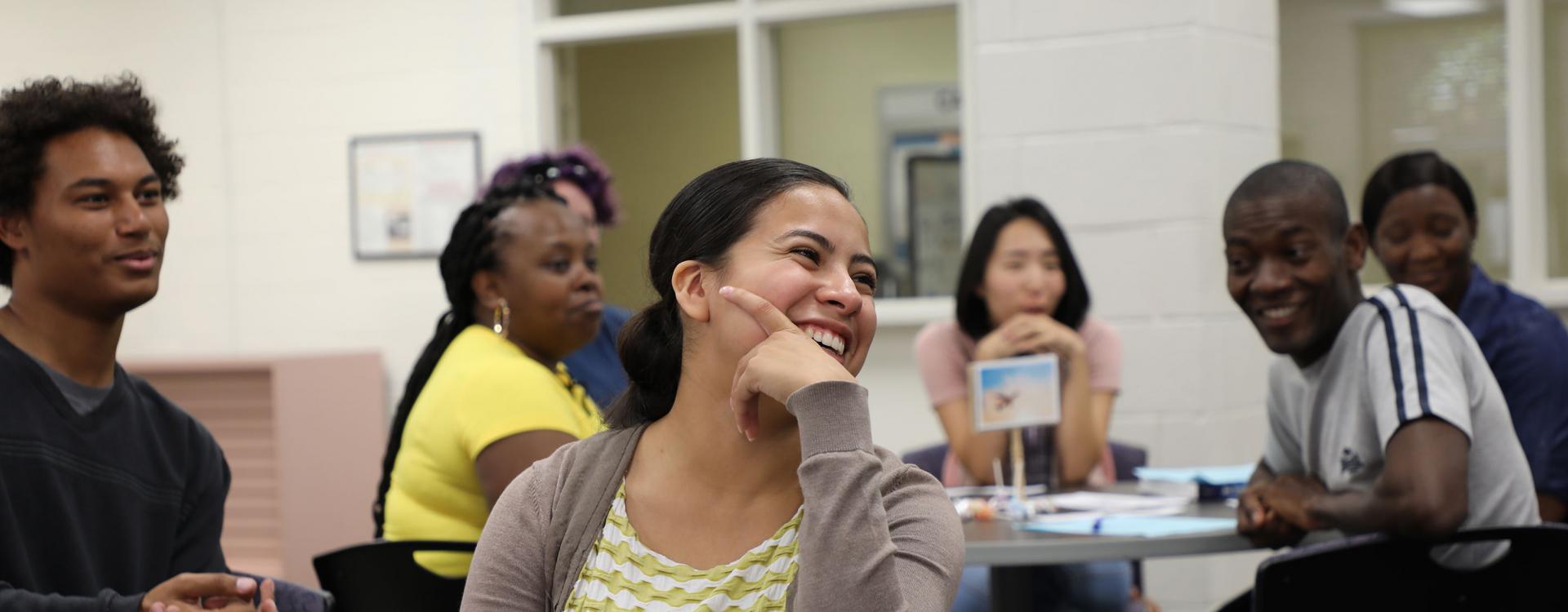 students sitting around tables in classroom with student in foreground laughing and smiling