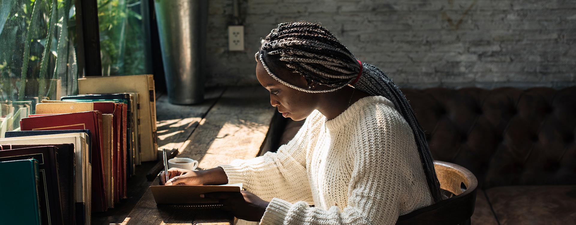 student writing in a journal at their desk with books sitting on it