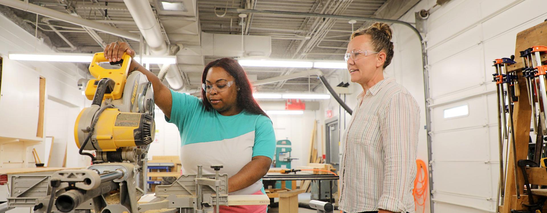 female student uses a circular saw while instructor supervises