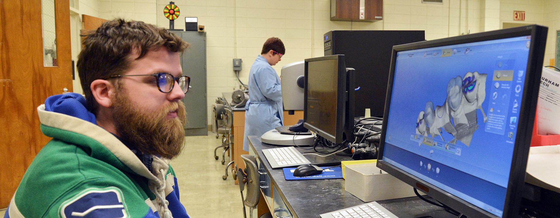 student in dental lab views 3-D image of jaw and teeth on computer screen