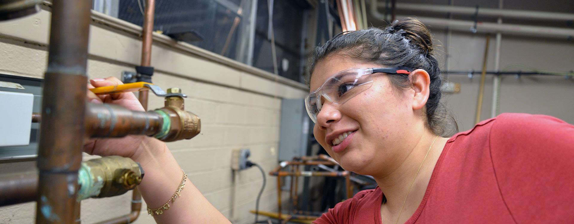 student working on plumbing with a wrench in HVAC class