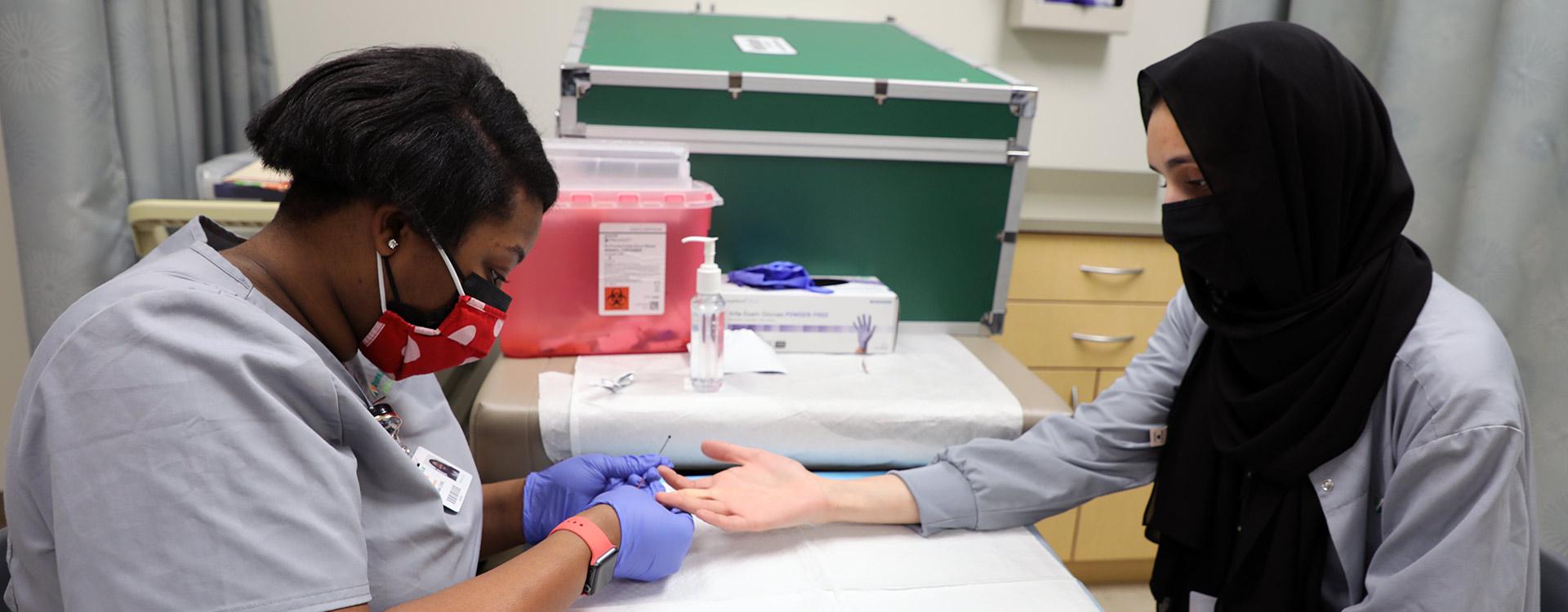 medical assisting student practices doing finger sticks on fellow student