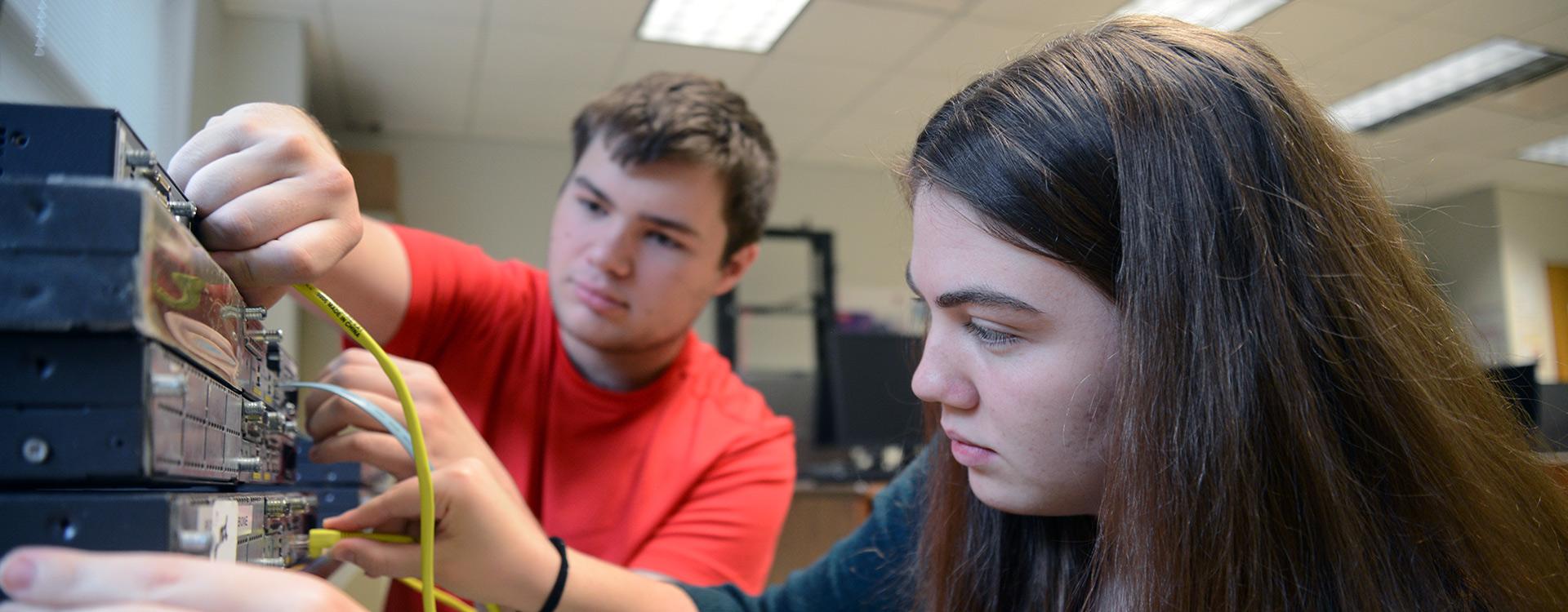 students plug in computer server cables while setting up a network