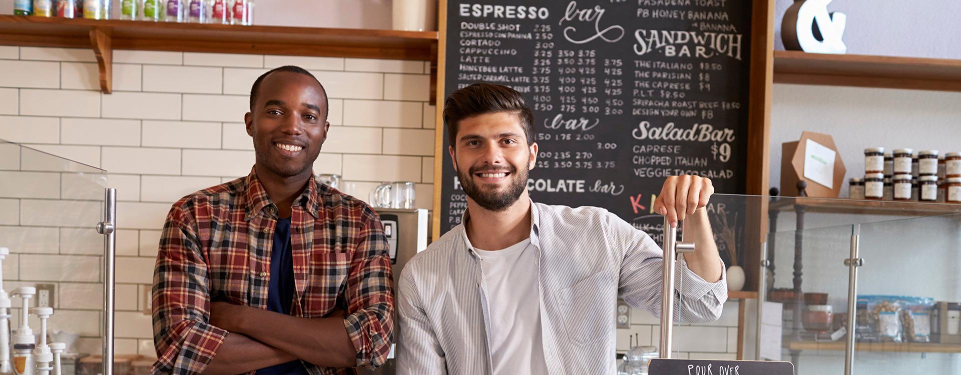 two business owners pose behind the counter in a sandwich shop