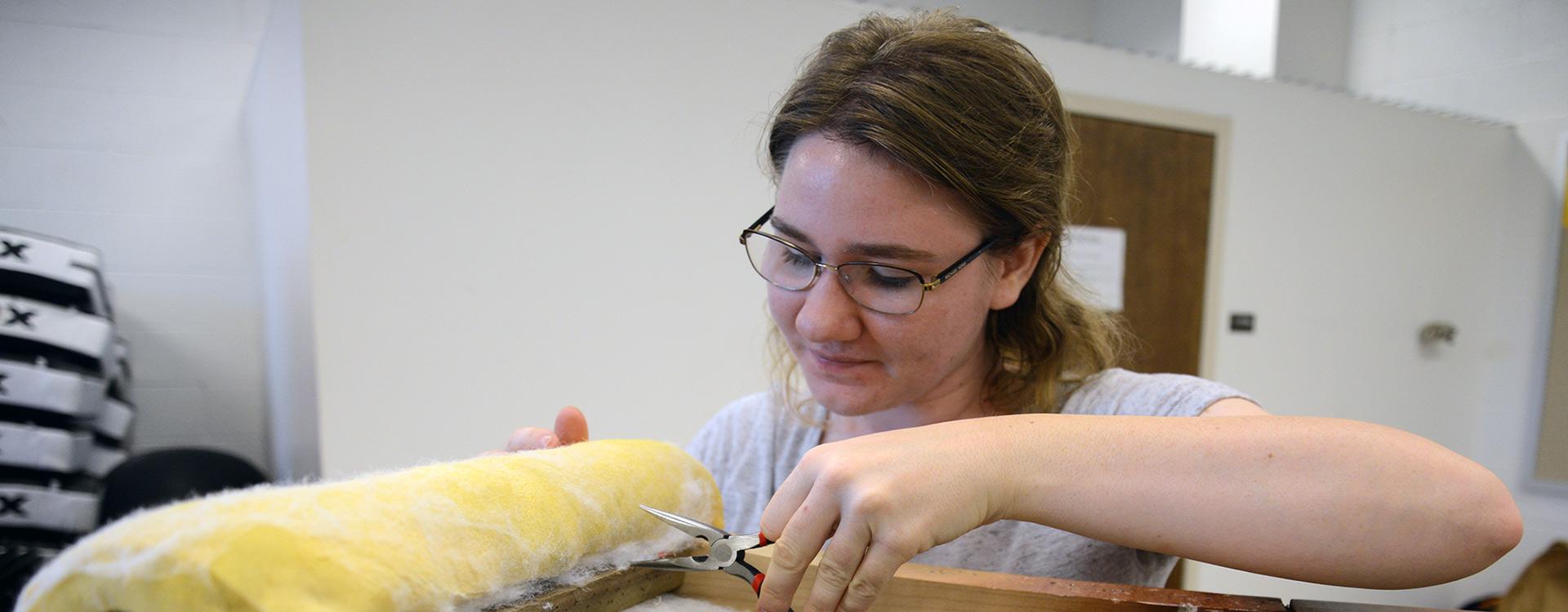 student pulls staples from a piece of furniture