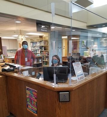 Charles Farrow, standing, and Meredith Lewis, seated, both masked,pictured at the circulation desk