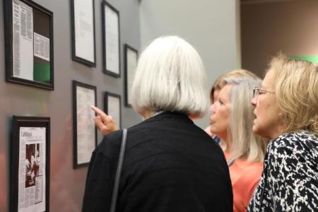 A group examines old newspaper clippings about the Durham Tech Clinical Trials Research Associate Program during its 25th anniversary celebration.
