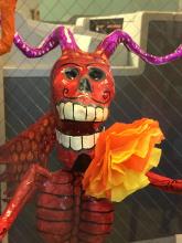 Red skeleton demon holding a flower in his mouth.