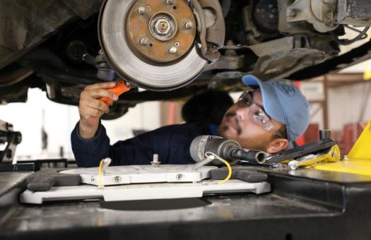 A student working under a car to repair a rotor