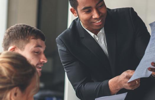 A businessperson holds a document in front of a group during a meeting.