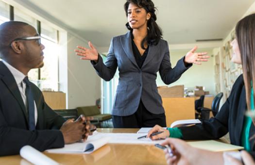 A business person stands in front of a group during a board meeting.