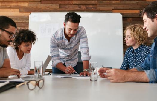 A business owner holds a pen while looking at a document while four employees watch him.