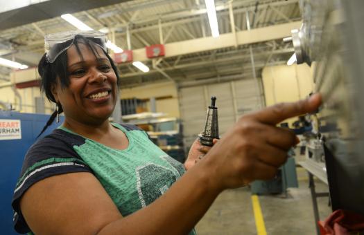 student in machining class wearing goggles on her head and pushing button on machine
