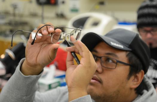 student holding up a pair of glasses and looking at them closely