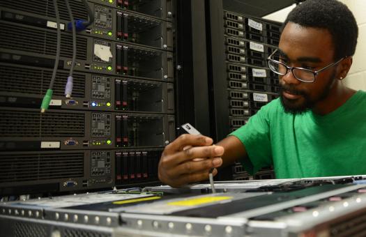 student in green shirt looking down at piece of computer equipment
