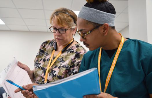 A male Durham Tech student points with a pen in his right hand to an EKG chart held by the EKG class instructor.
