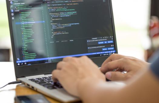 person typing on laptop with colorful computer code visible on the screen