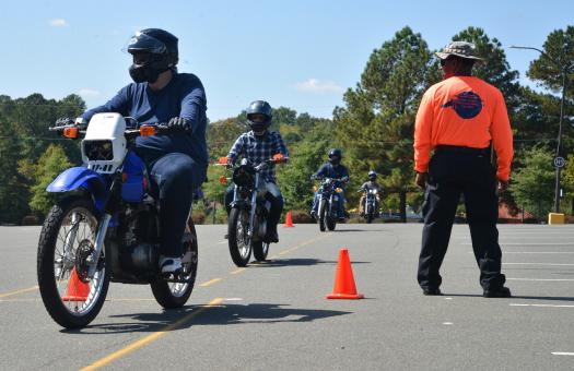 motorcyclists drive around orange cones while instructor supervises