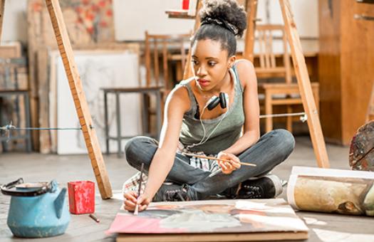 female student sitting on floor painting a still life