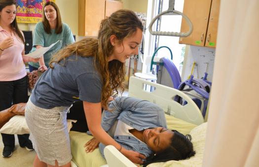 student leaning over bed to help other student lift themselves up
