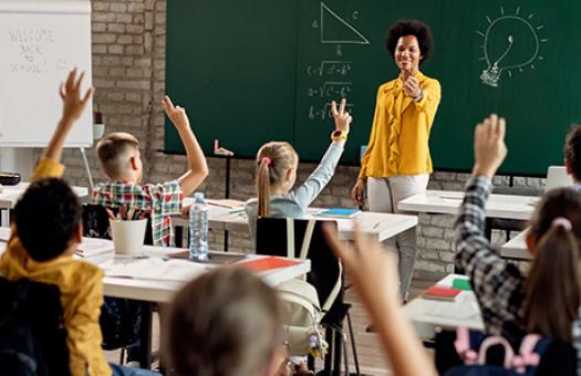 teacher standing in front of class calls on students with their hands raised