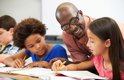 smiling teacher assisting elementary student with an assignment