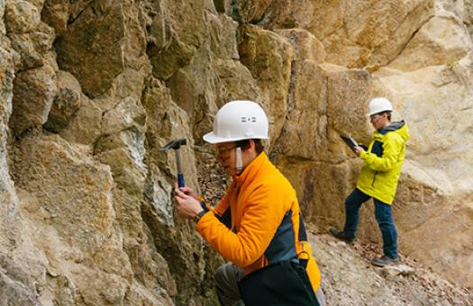 geologist chipping and examining rocks from a cliff face