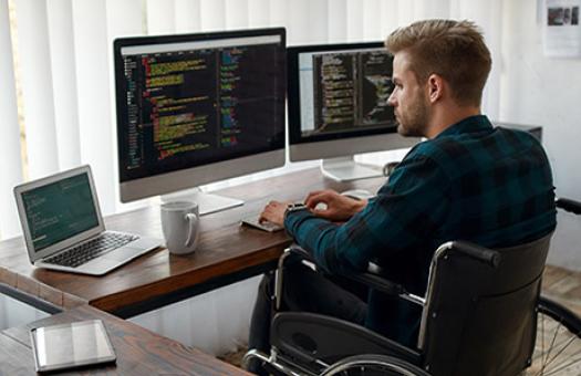 student in a wheelchair works at computer desk with dual monitors