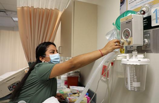 nursing student reaches above bed to adjust suction equipment