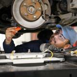 A student working under a car to repair a rotor