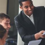 A businessperson holds a document in front of a group during a meeting.
