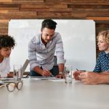 A business owner holds a pen while looking at a document while four employees watch him.