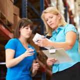 A manager holds a clipboard and a box in front of an employee.