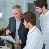 A hotel manager points to a piece of paper as two employees look on.