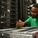 student in green shirt looking down at piece of computer equipment