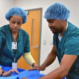 A male and female student wearing medical scrubs carefully lift a cloth sheet during a Central Sterile Processing class at Durham Tech.